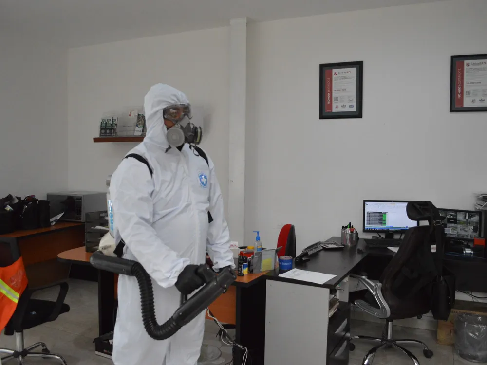 Técnico de Grupo CCN sanitizando una oficina con certificados ISO 9001 y 45001 de fondo
